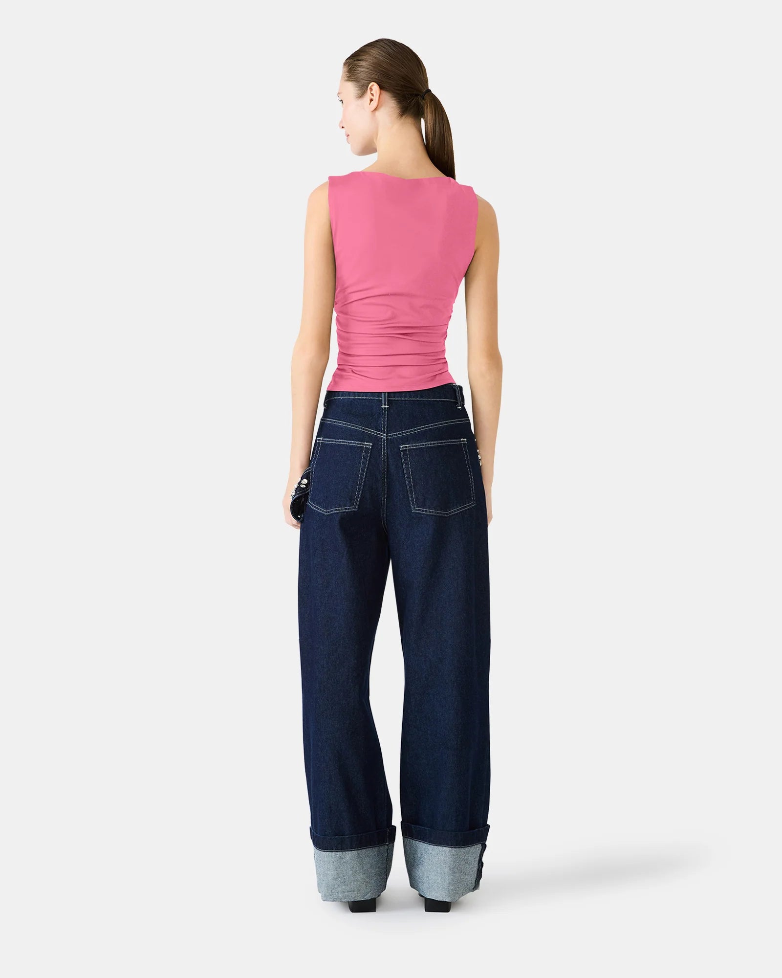 Woman wearing a pink sleeveless top and blue jeans on a white background