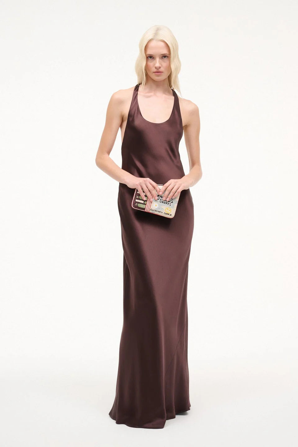 Woman wearing a brown halter neck dress holding a colorful clutch on a white background