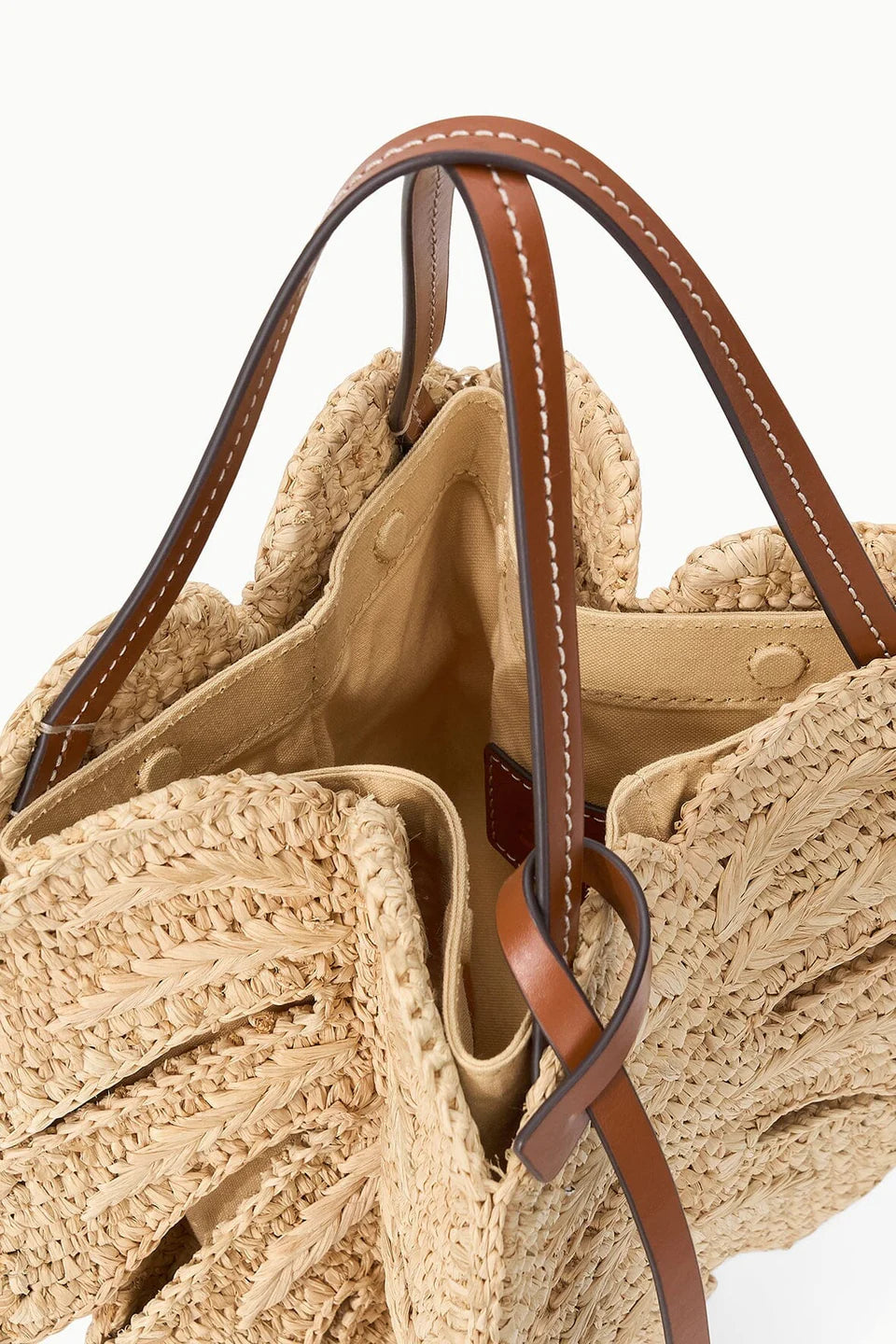 Close-up of a straw bag with brown leather handles and trim on a white background