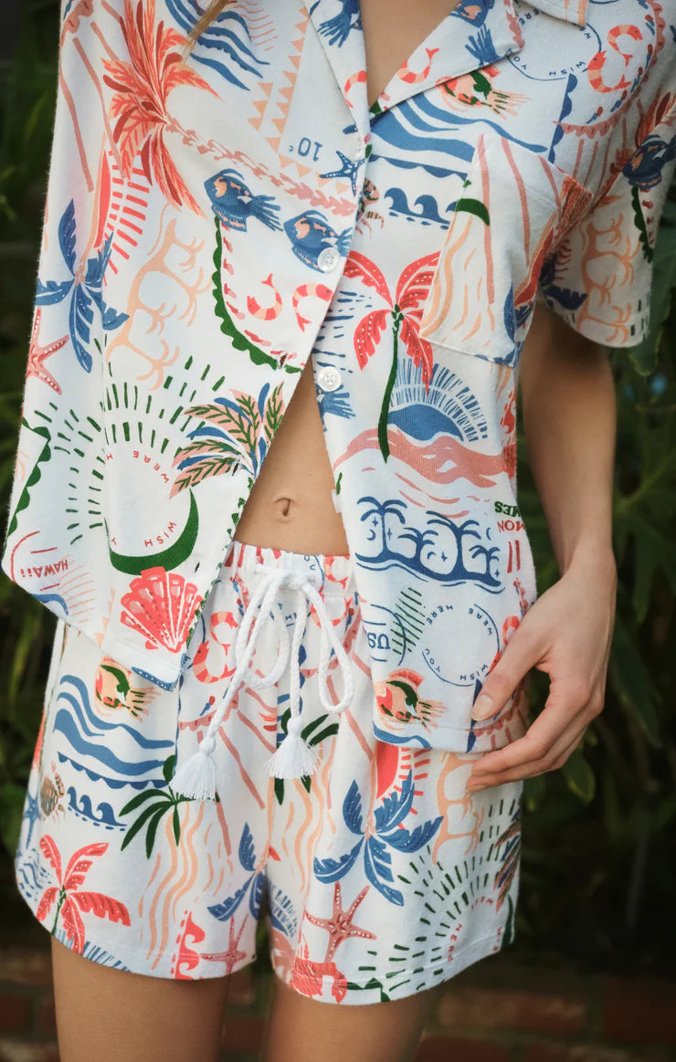 Person wearing a colorful tropical-themed shirt and shorts set with a blurred background.