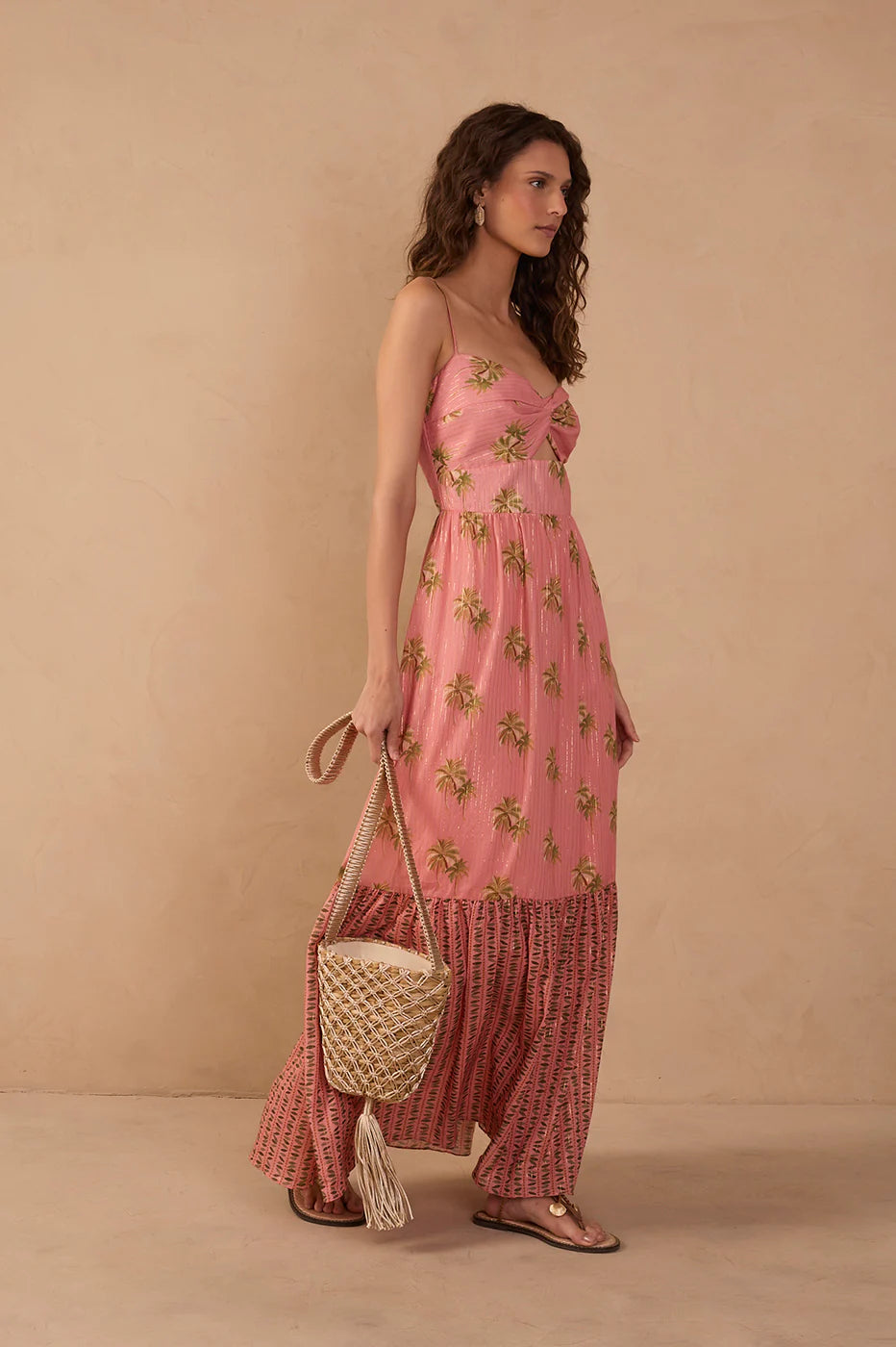 Woman wearing a pink floral dress holding a woven bag against a beige background