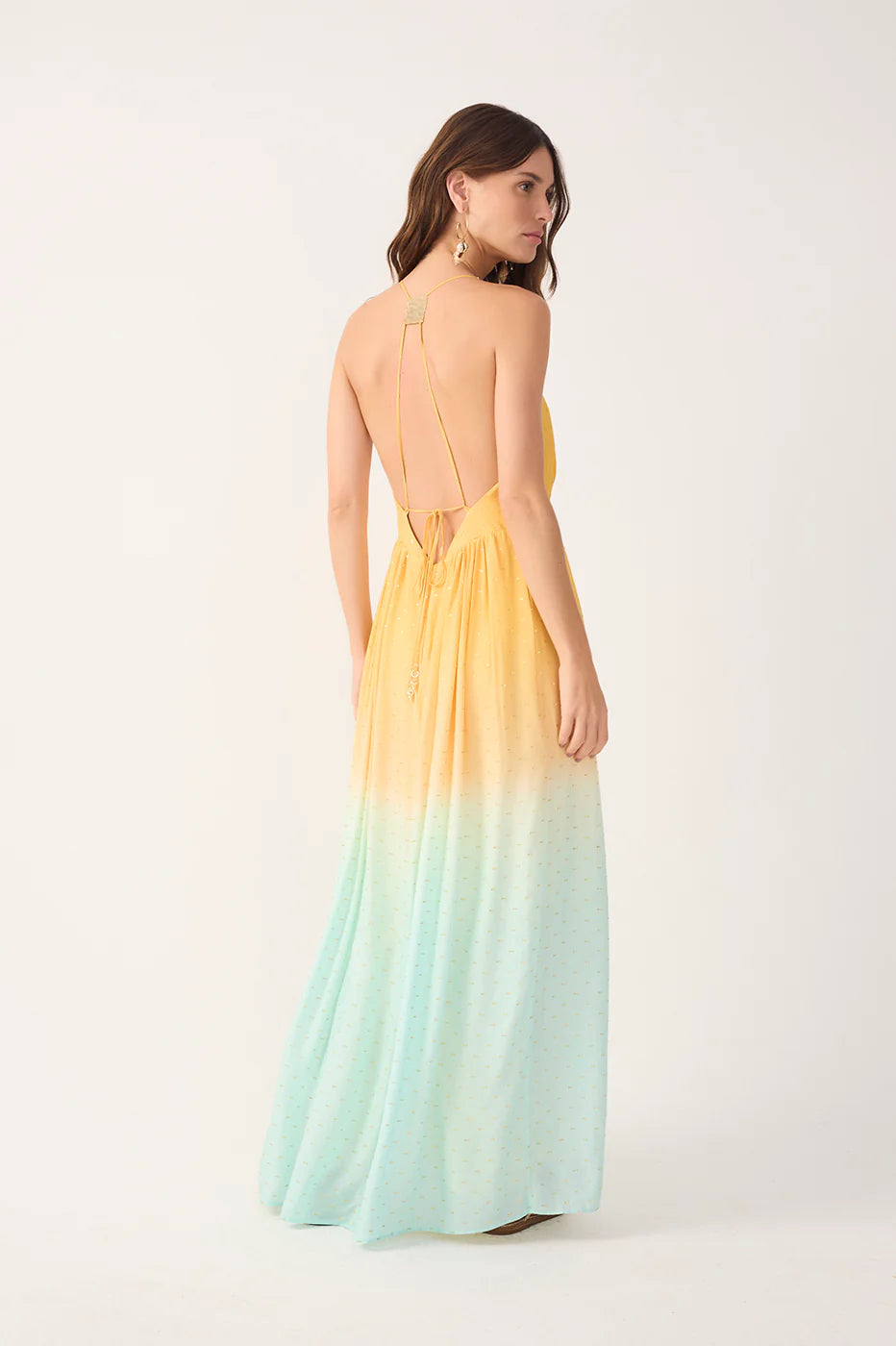 Woman wearing a yellow to light blue gradient dress with an open back on a white background