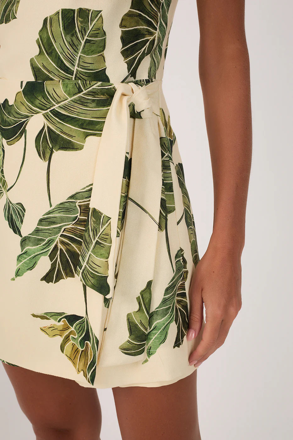 Beige dress with green leaf pattern worn by a person on a white background