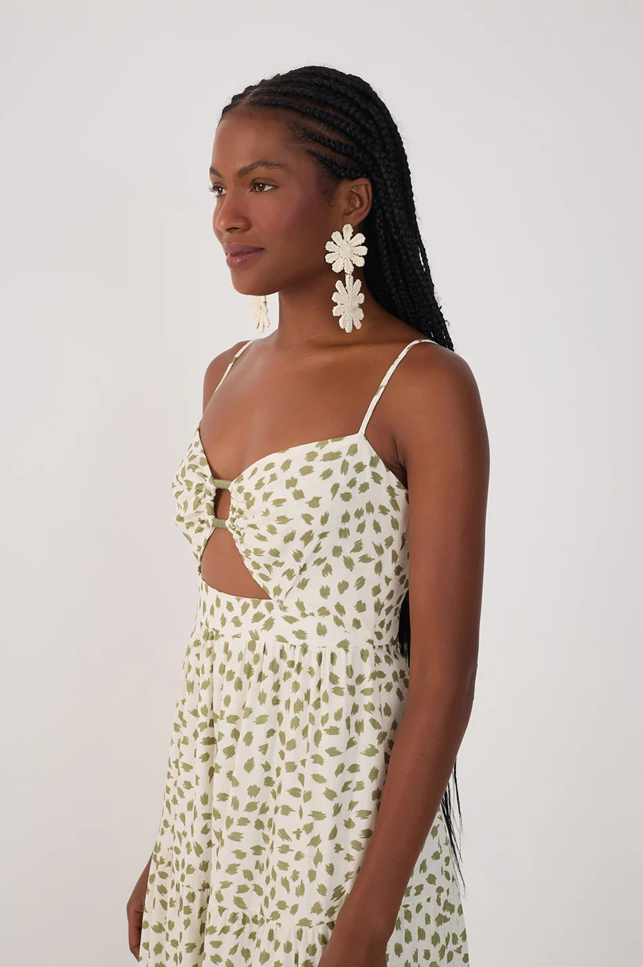 Woman wearing a white dress with green floral pattern and floral earrings against a plain background