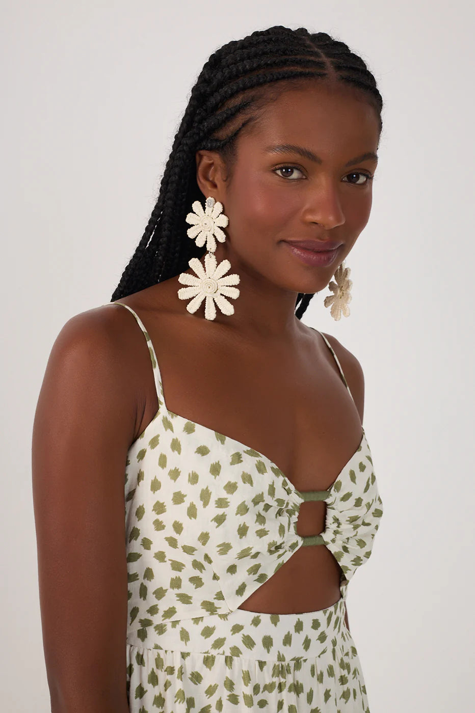 Woman wearing a floral dress with cut-out design and large white earrings against a white background