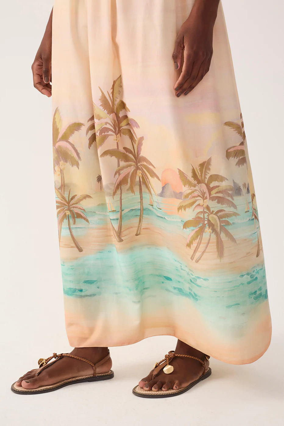 Person wearing a long dress with a palm tree and beach design, standing on a white background.