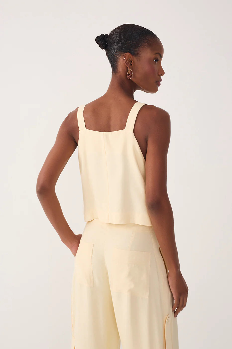 Woman wearing a light yellow sleeveless top and high-waisted pants against a white background