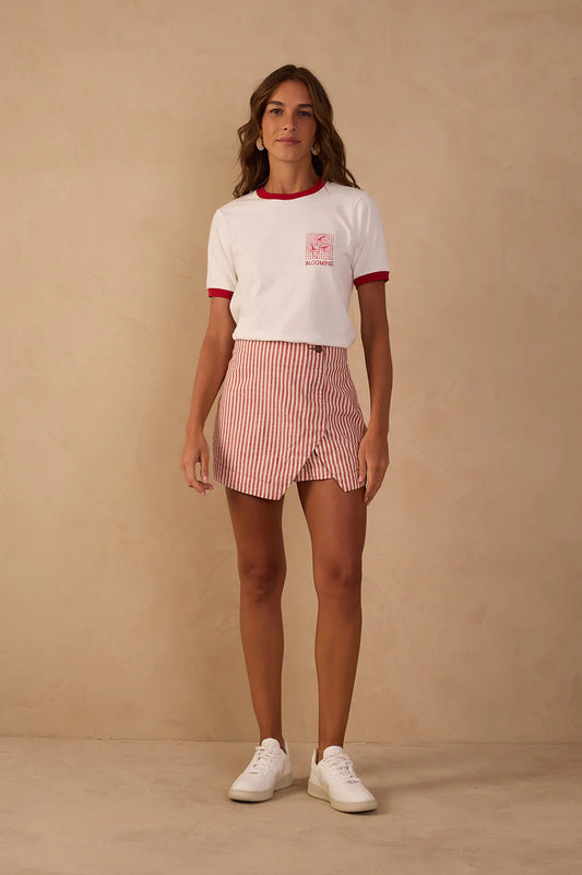 Woman wearing a white t-shirt with red trim and a striped pink skirt against a beige background