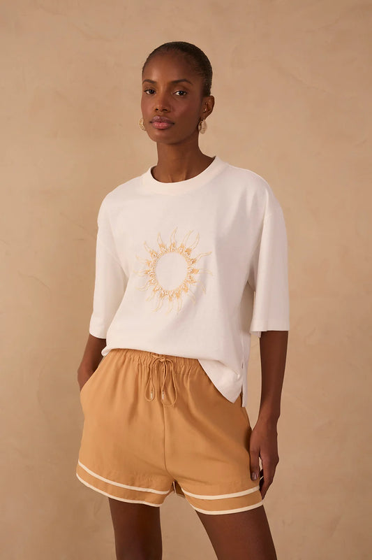 Woman wearing a white sweater with a sun design and beige shorts on a beige background