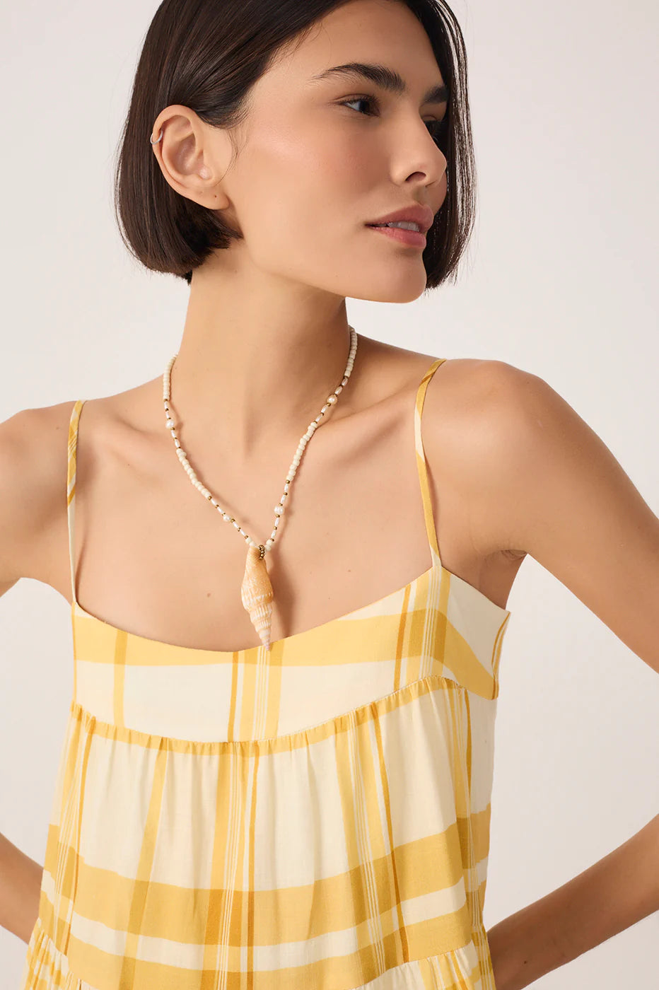 Woman wearing a yellow and white checkered dress with a necklace on a plain background