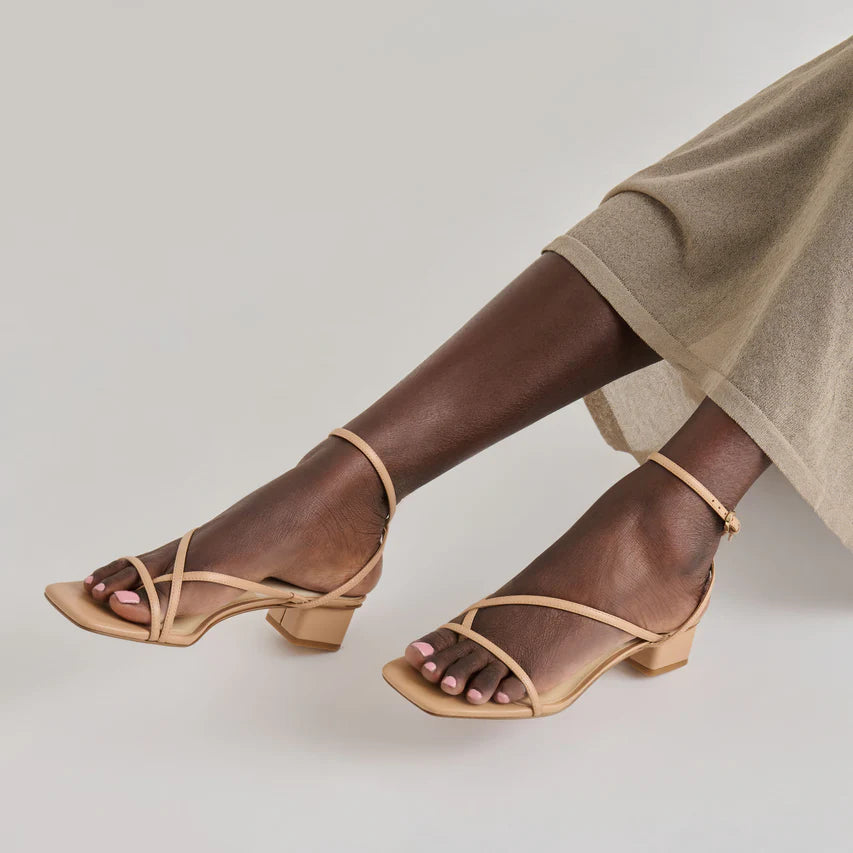 Brown sandals worn with a beige skirt on a neutral background