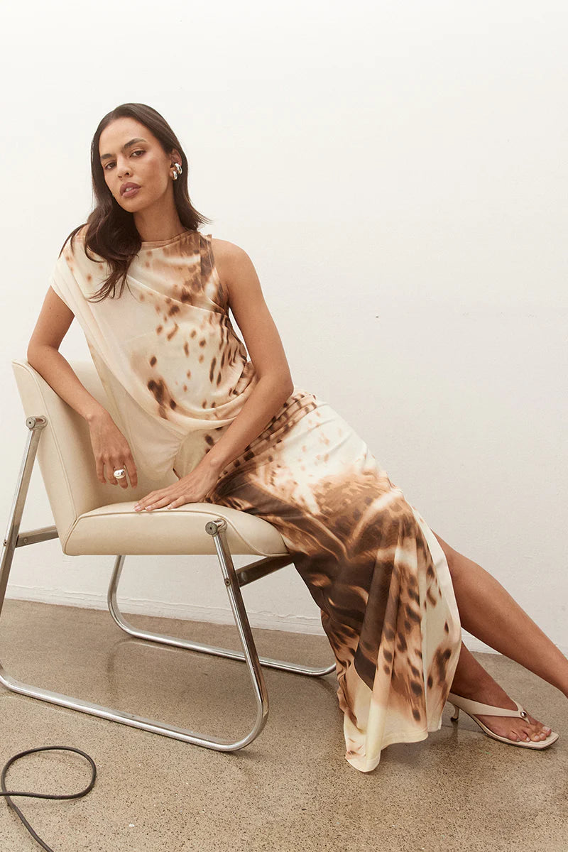 Woman sitting on a chair wearing a tie-dye dress with a neutral background