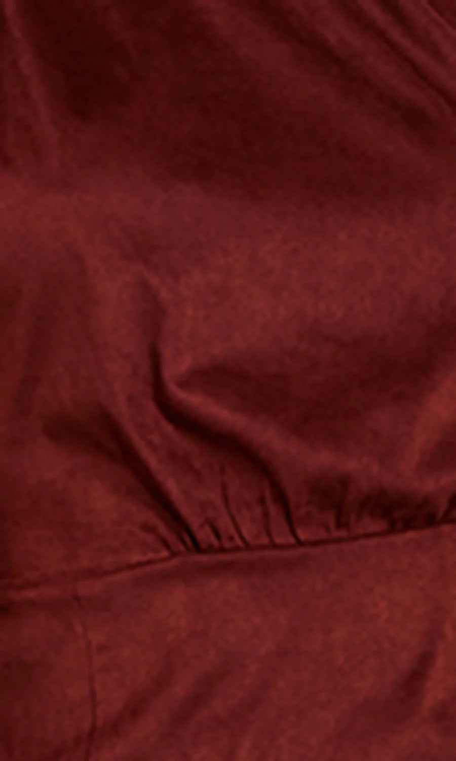 A close-up of a dark red or burgundy textured fabric with soft folds and a gathered seam.
