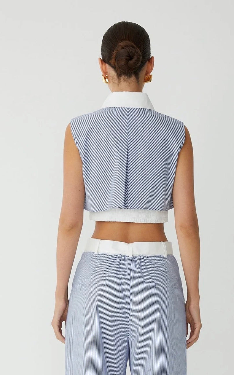 A model shown from the back wearing a light blue and white striped sleeveless crop top with a white collar, paired with matching striped trousers.