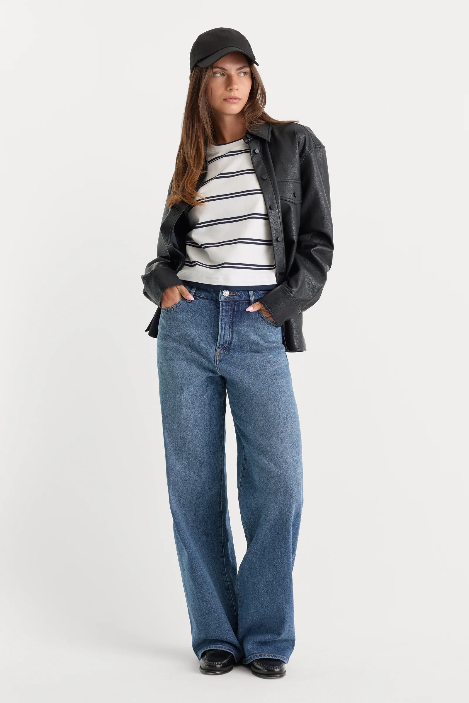 Person wearing a black jacket, striped shirt, and blue jeans on a white background