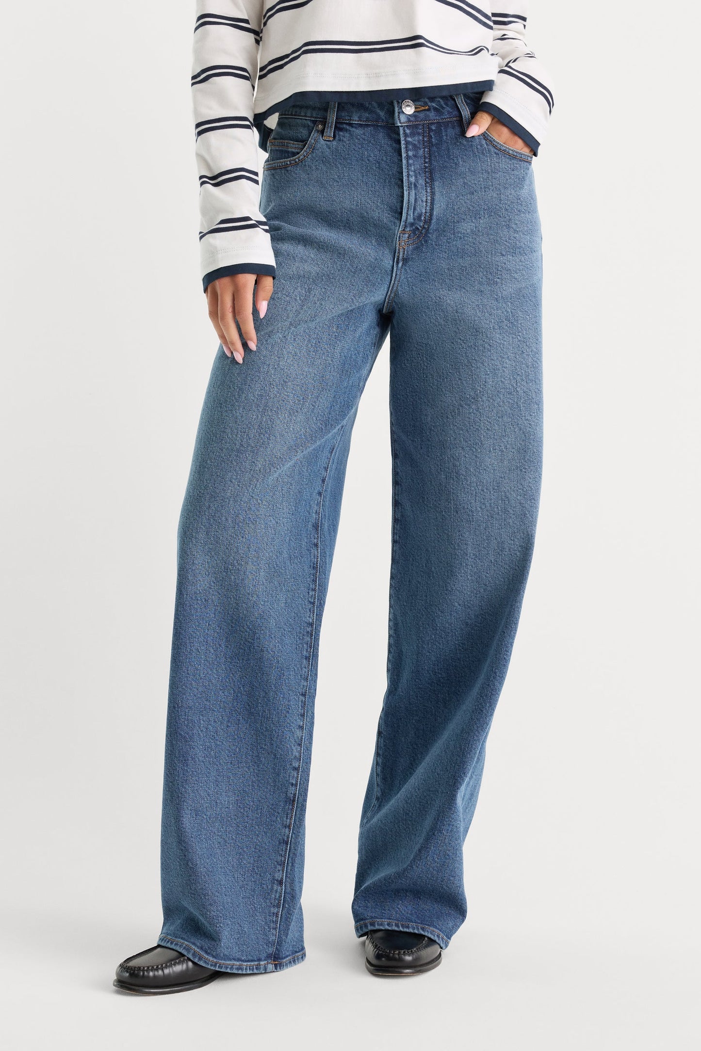 Person wearing blue jeans and a striped shirt on a white background