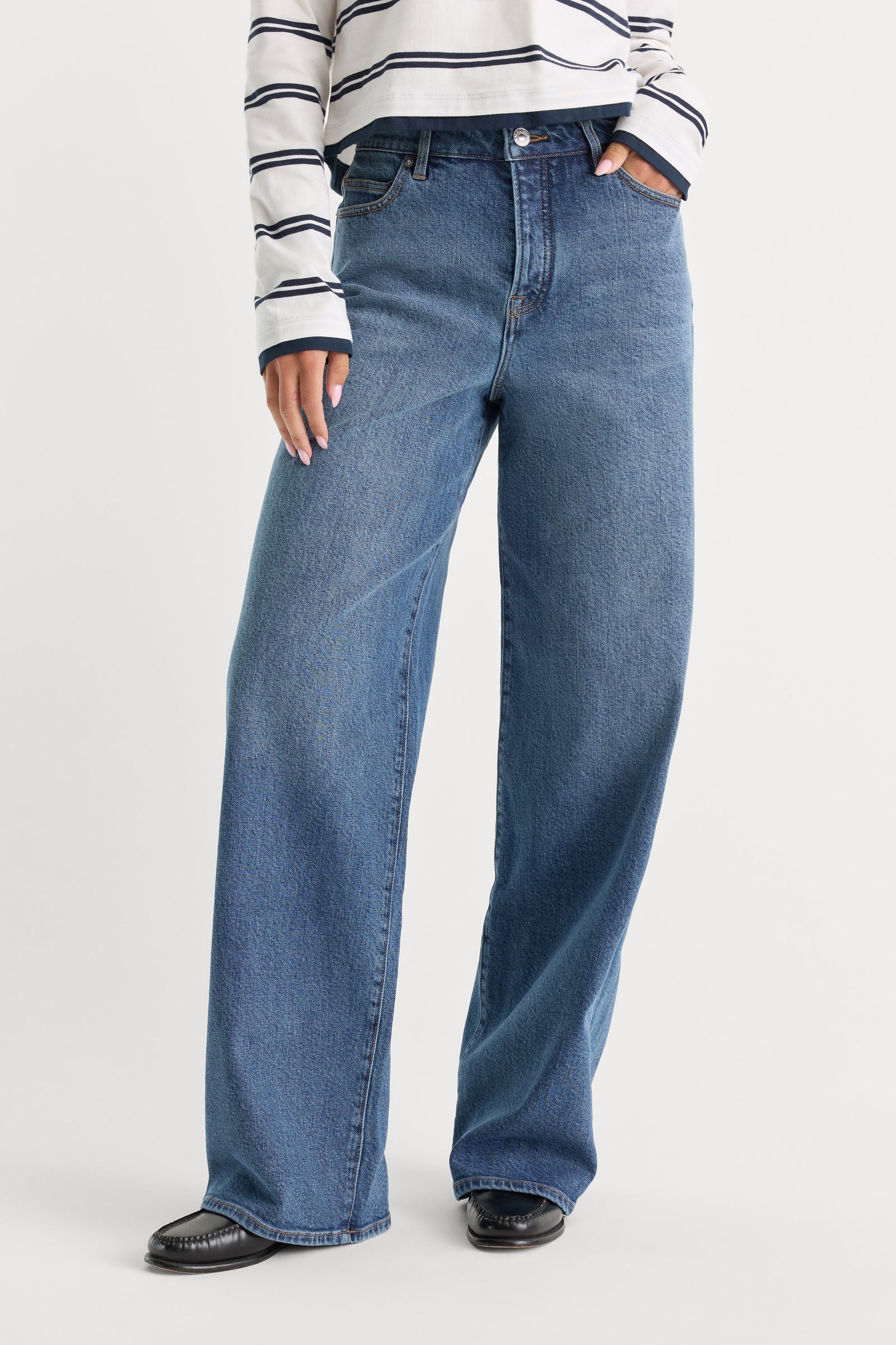 Person wearing blue jeans and a striped shirt on a white background