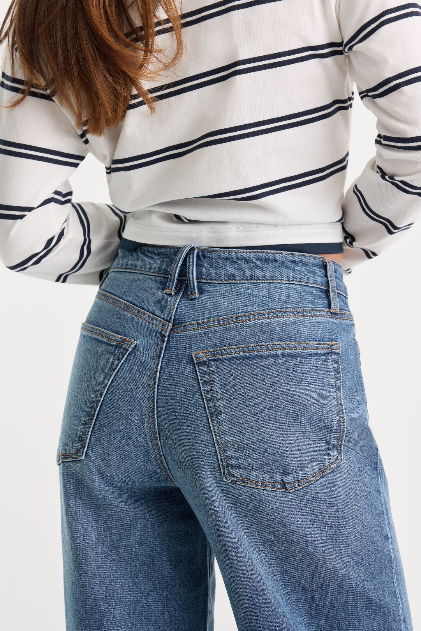 Person wearing a striped shirt and blue jeans on a white background