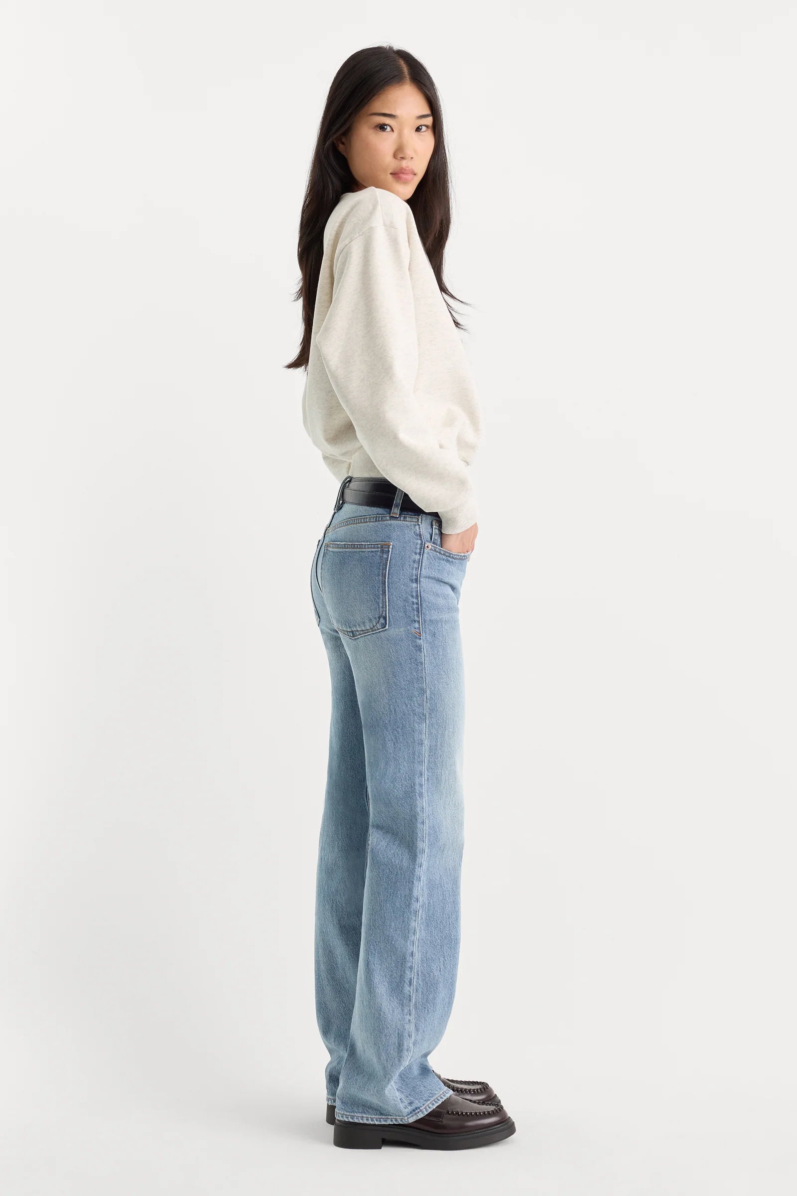 Woman wearing a white sweater and light blue jeans on a white background