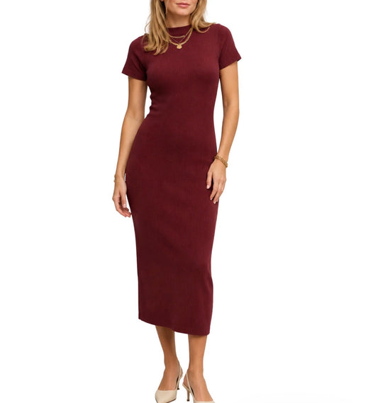 A woman modeling a short-sleeve, bodycon midi dress in a deep burgundy color, paired with beige high heels and gold jewelry, against a plain white background.