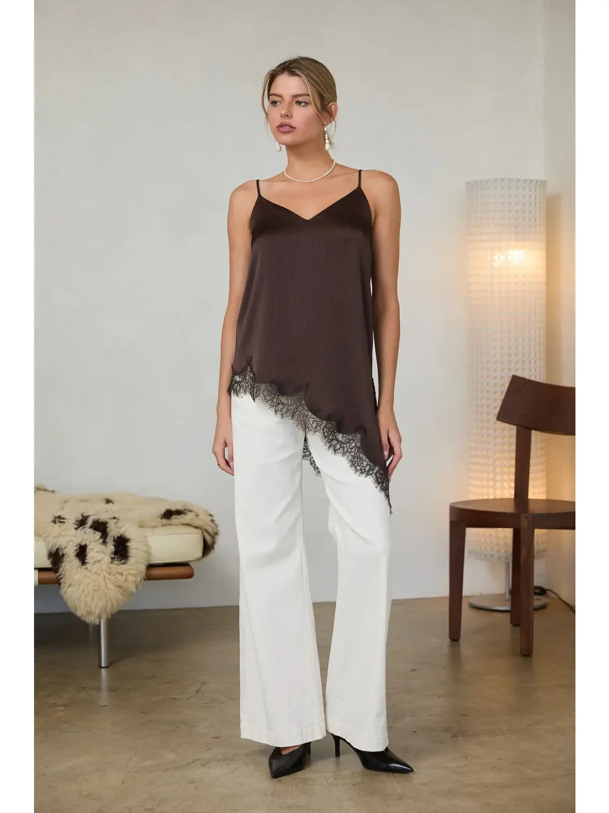 Woman wearing a brown top and white pants in a minimalistic room.