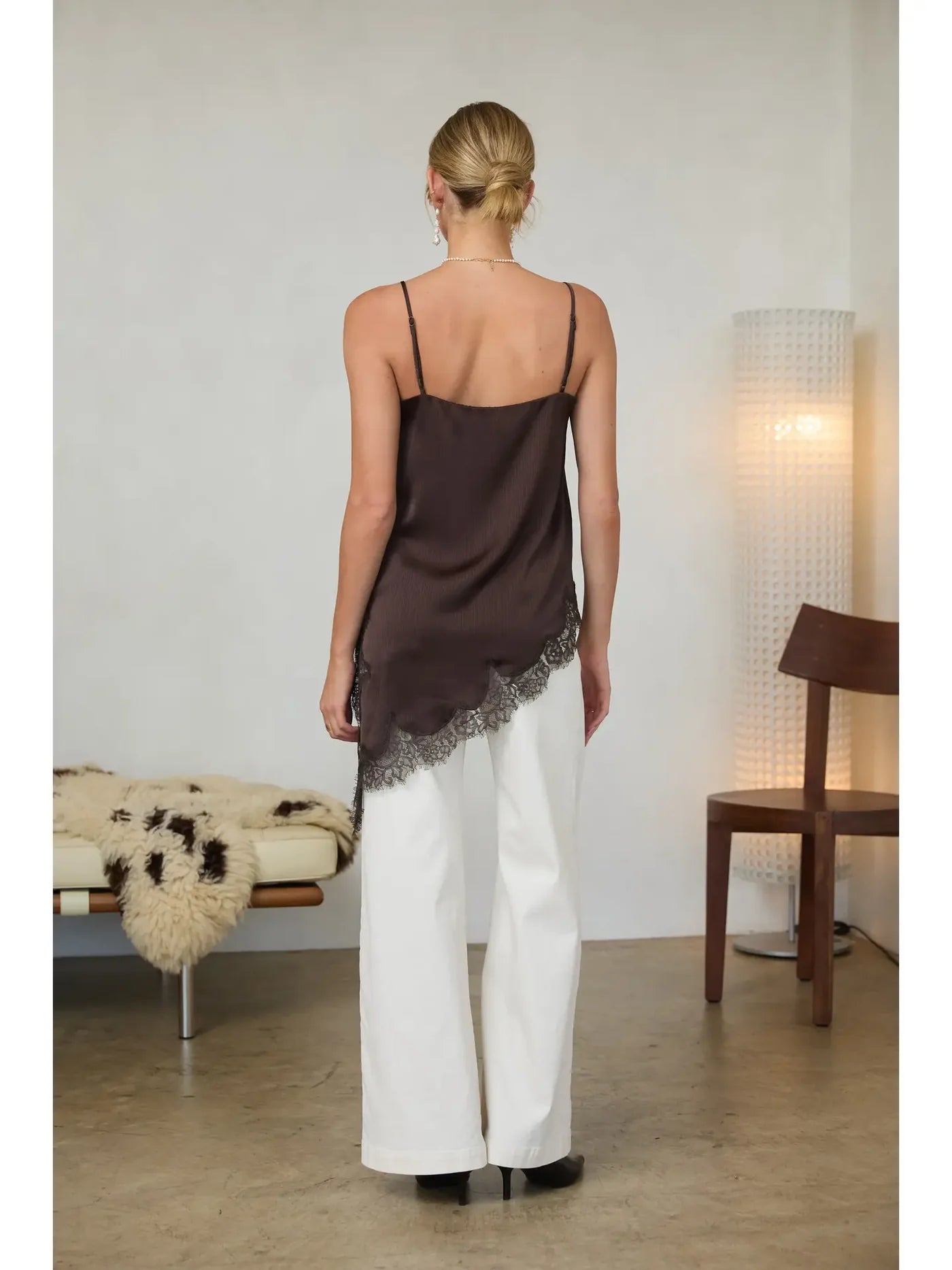Woman wearing a brown top and white pants in a minimalistic room.