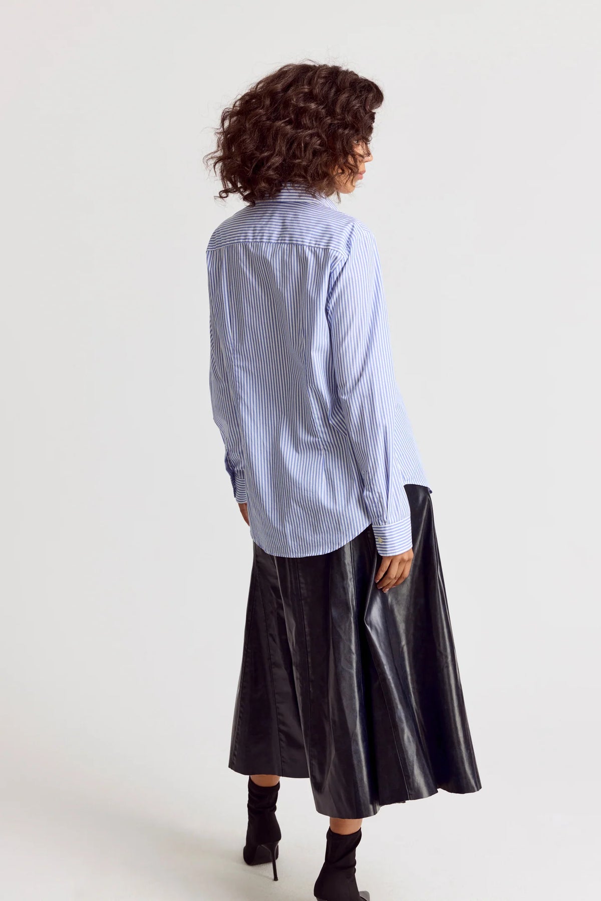 Person wearing a light blue striped shirt and black skirt on a white background
