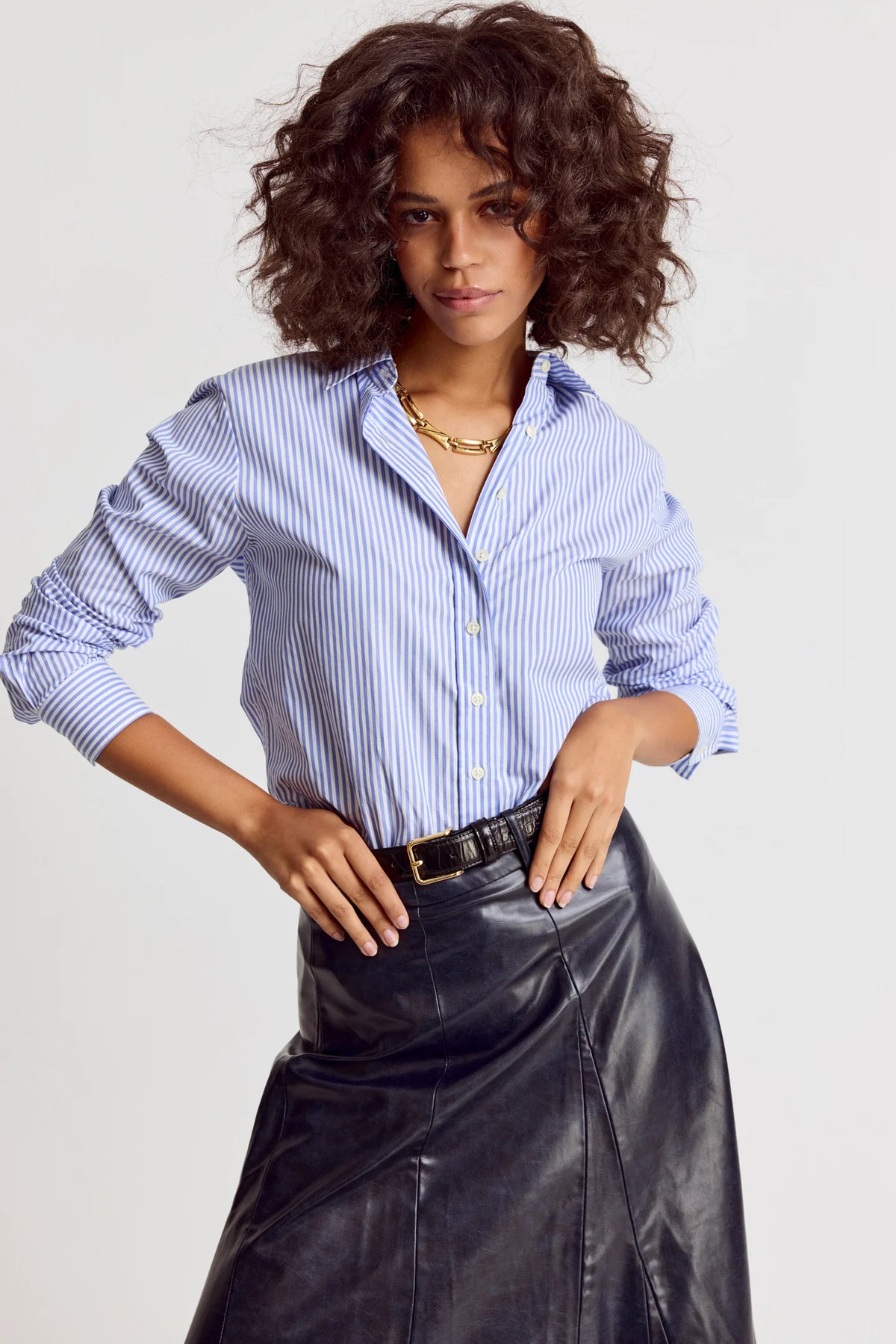 Woman wearing a blue striped shirt and black leather skirt on a light gray background