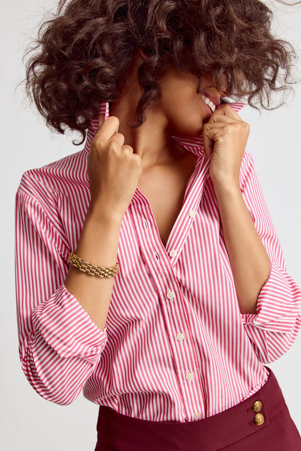Person wearing a pink and white striped shirt with a blurred face on a light background