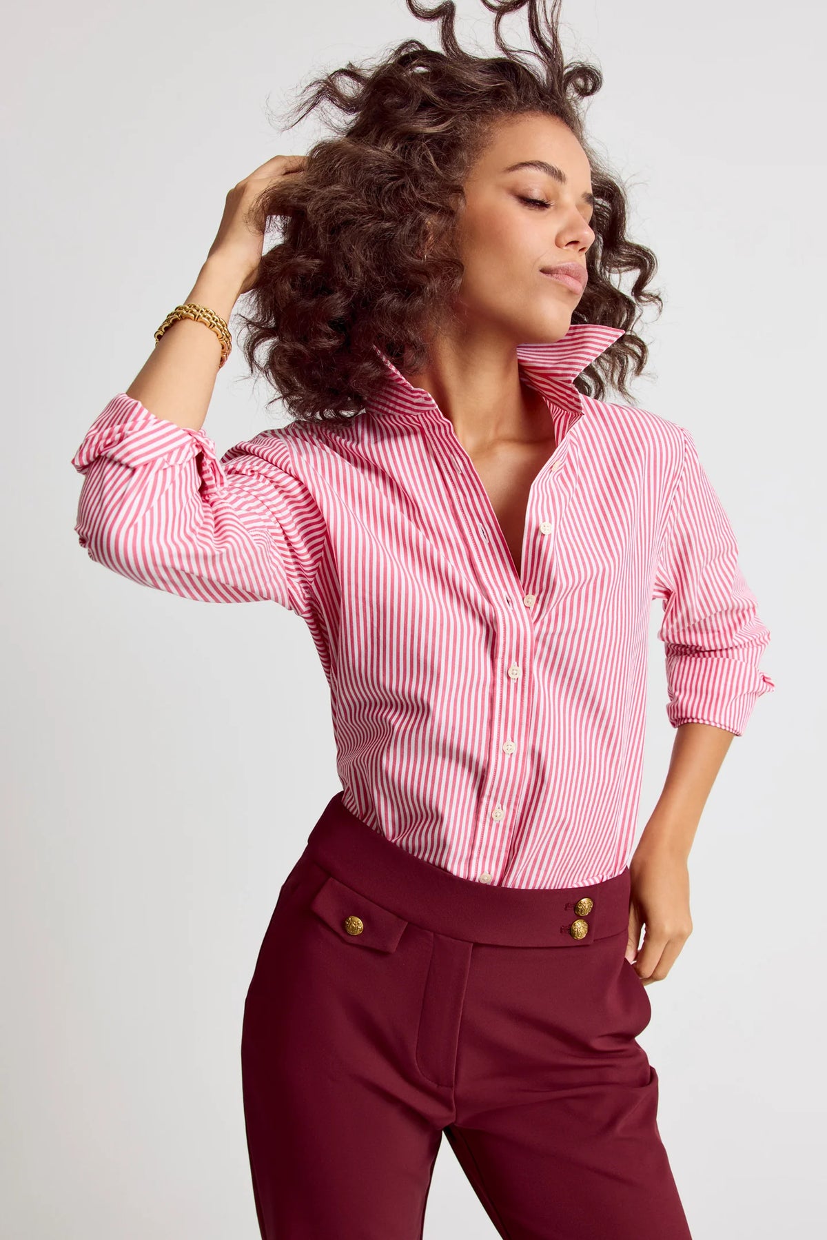 Woman wearing a pink and white striped shirt with burgundy pants on a light gray background