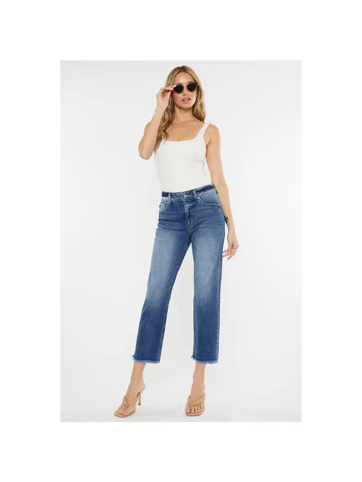 A female model wearing sunglasses and a white strapless top, paired with high-waisted cropped blue denim jeans with a frayed hem.