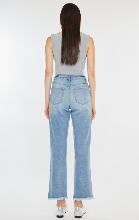 Person wearing light blue jeans with a frayed bottom hem and a gray top on a white background