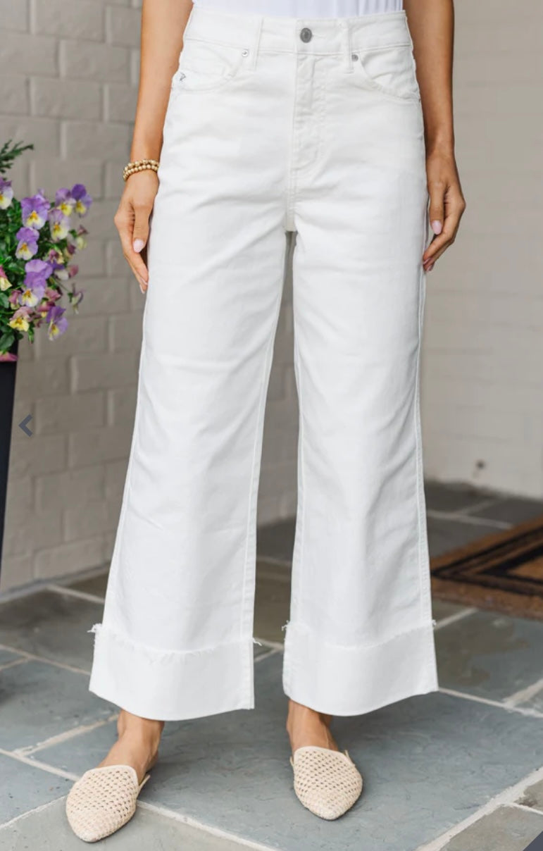 Person wearing white wide-leg jeans standing on a stone floor with a floral arrangement in the background.