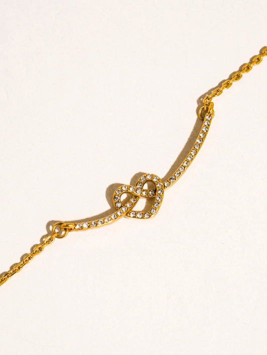 Gold necklace with a heart knot design on a light beige background