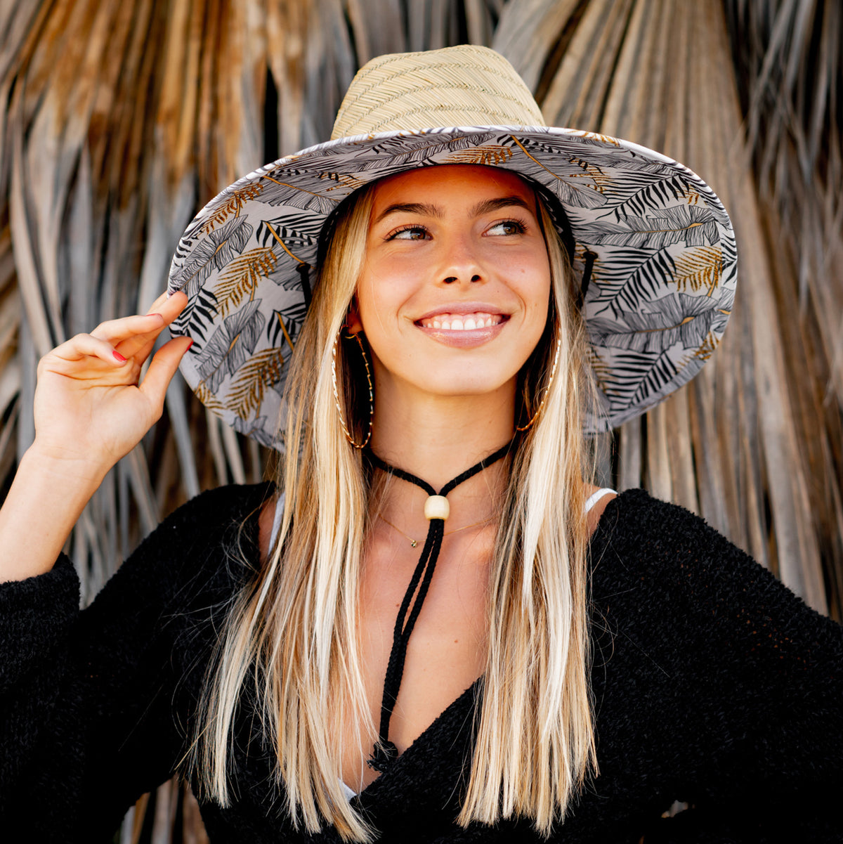 A person wearing a straw hat with a gold leaf pattern, featuring a wide brim and an adjustable chin cord.
