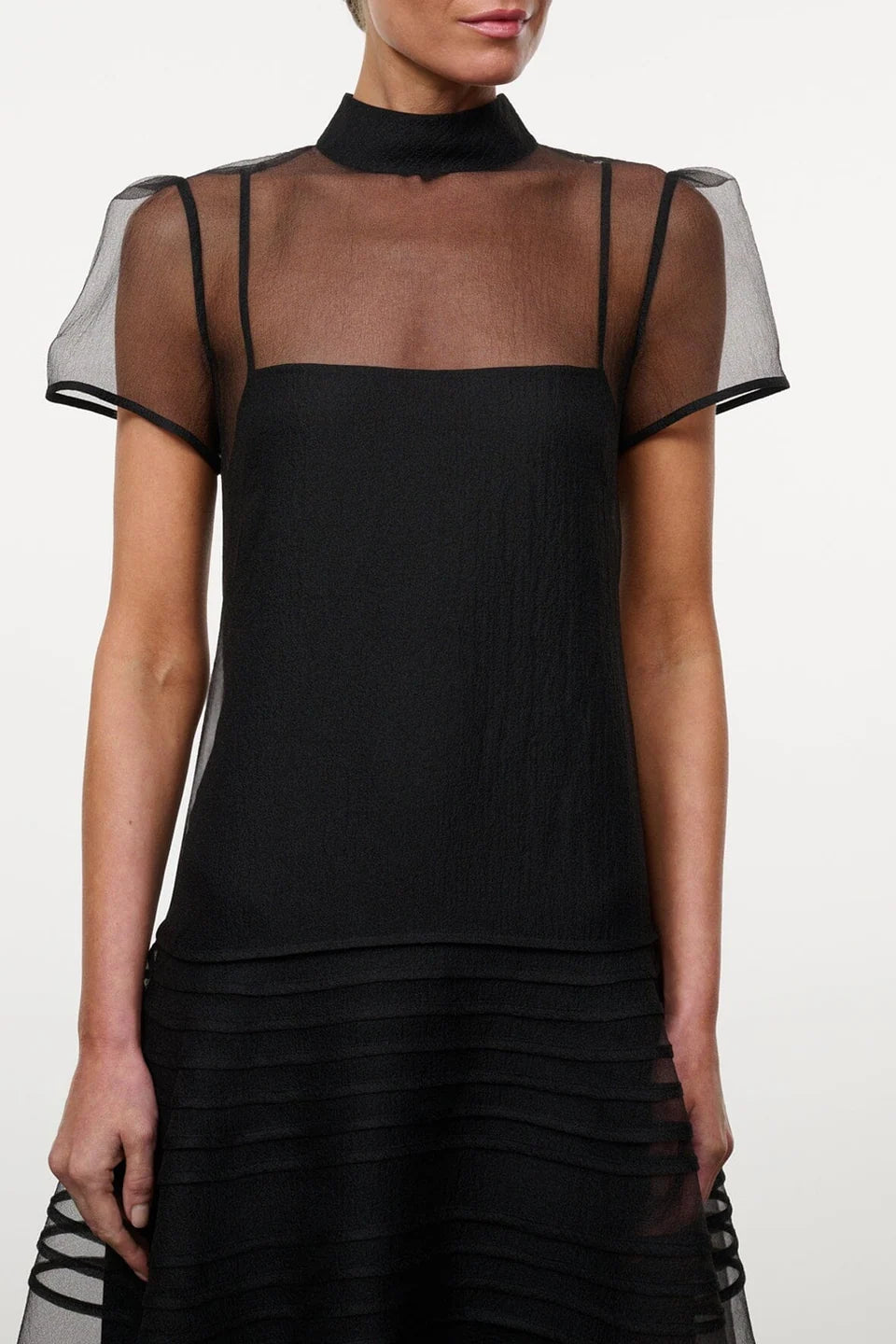 Model wearing the STAUD Stratton maxi dress that features a sheer outer layer with a black maxi slip underneath. The outer layer features a mock neckline and capped sleeves.