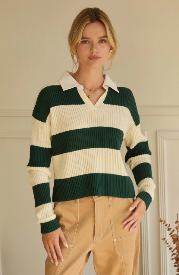 Woman wearing a green and cream striped sweater with beige pants indoors.