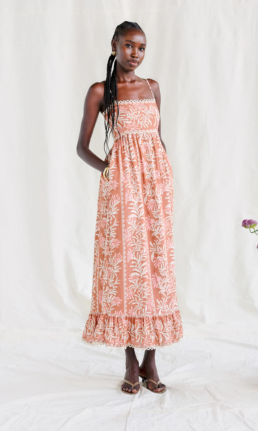 Woman wearing a coral sleeveless midi dress with white floral pattern on a white background