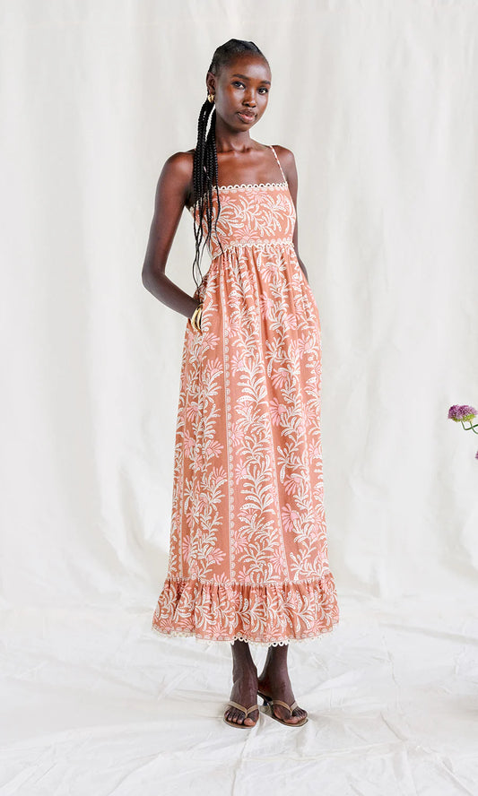 Woman wearing a coral sleeveless midi dress with white floral pattern on a white background