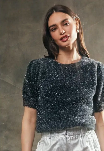 Woman wearing a dark blue gray glittery top against a gray background