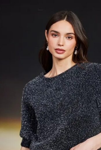 Woman wearing a dark gray textured sweater against a black background