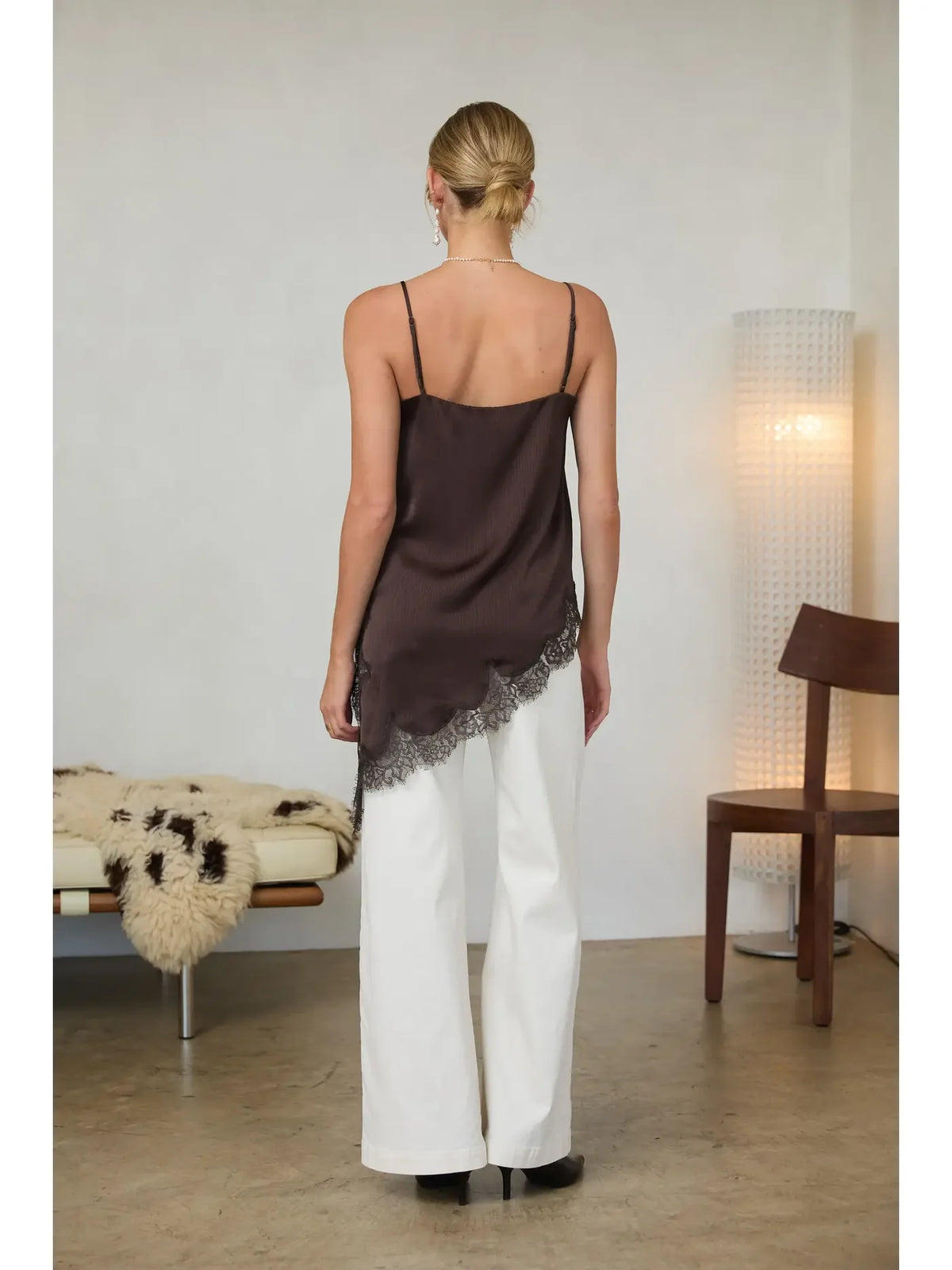 Woman wearing a brown top and white pants in a minimalistic room.
