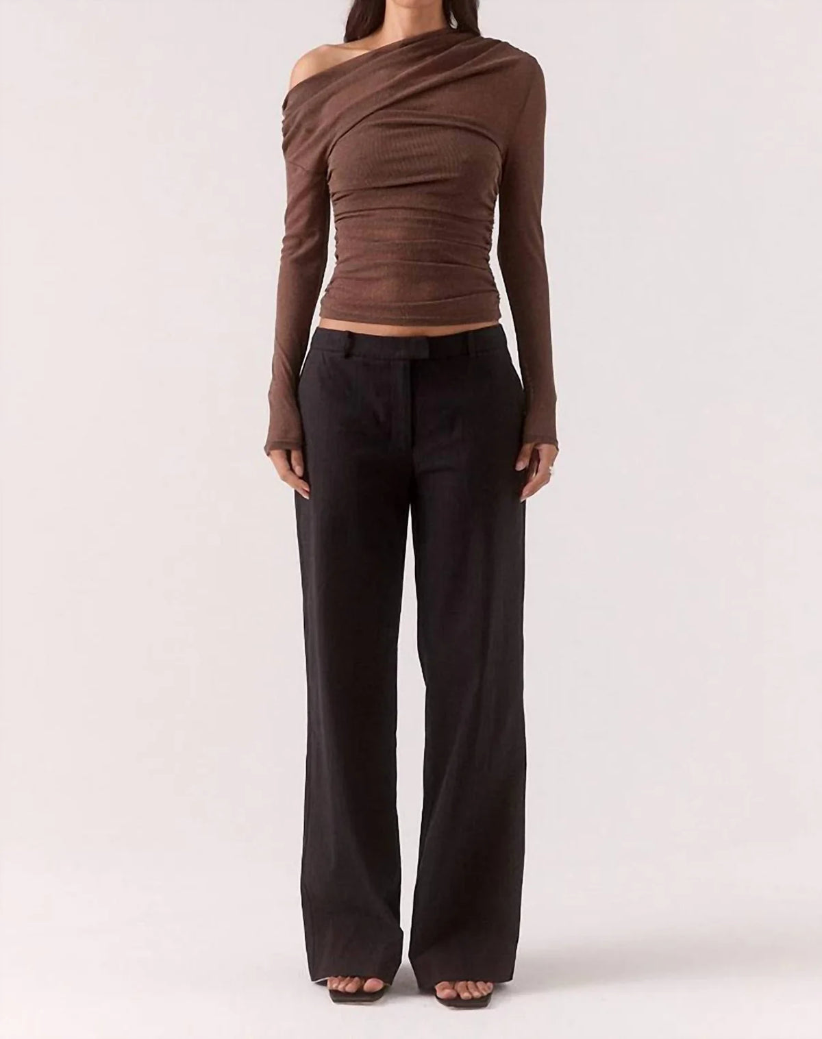 Woman wearing a brown off-shoulder top and black pants on a white background