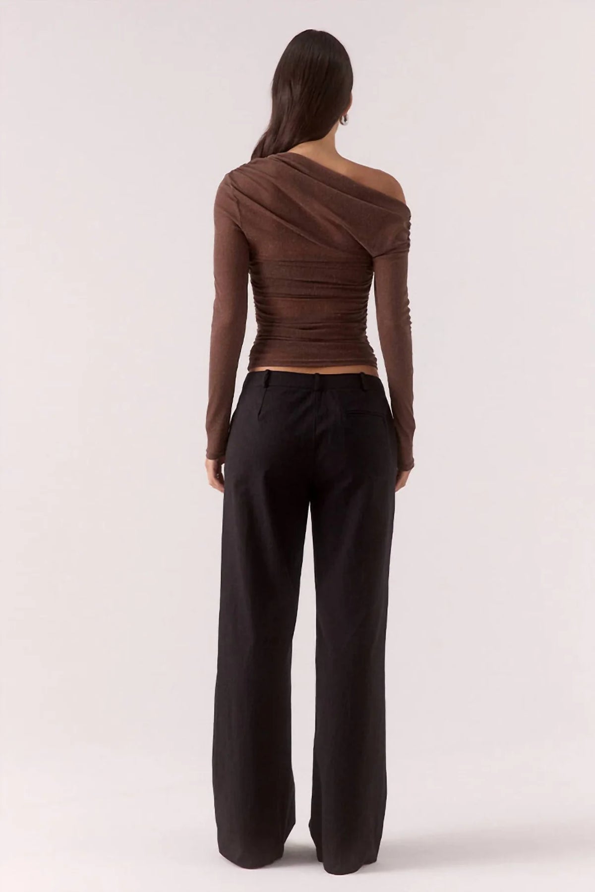 Person wearing a brown one-shoulder top and black pants on a white background