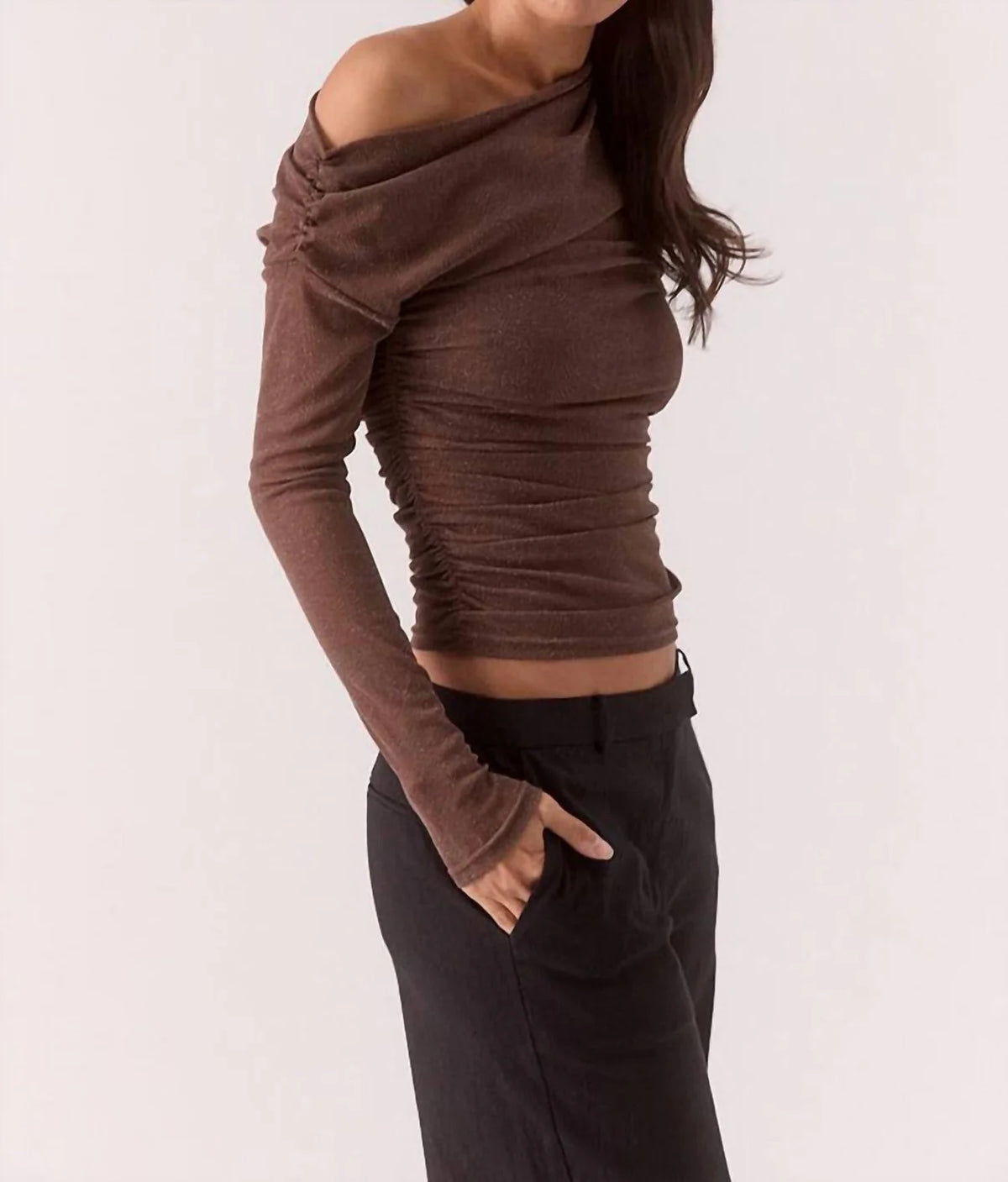 Woman wearing a brown off-shoulder top and black pants on a white background