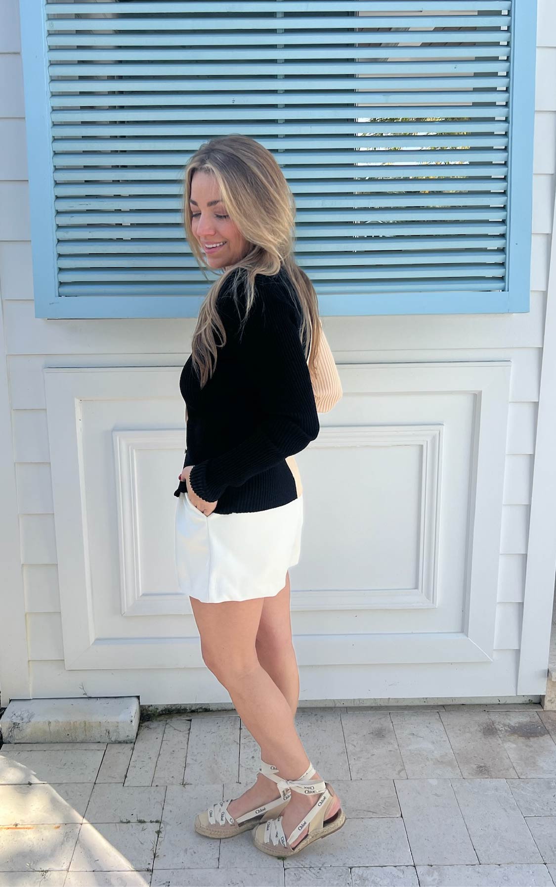 Woman wearing a black sweater and white shorts standing infront of a white wall