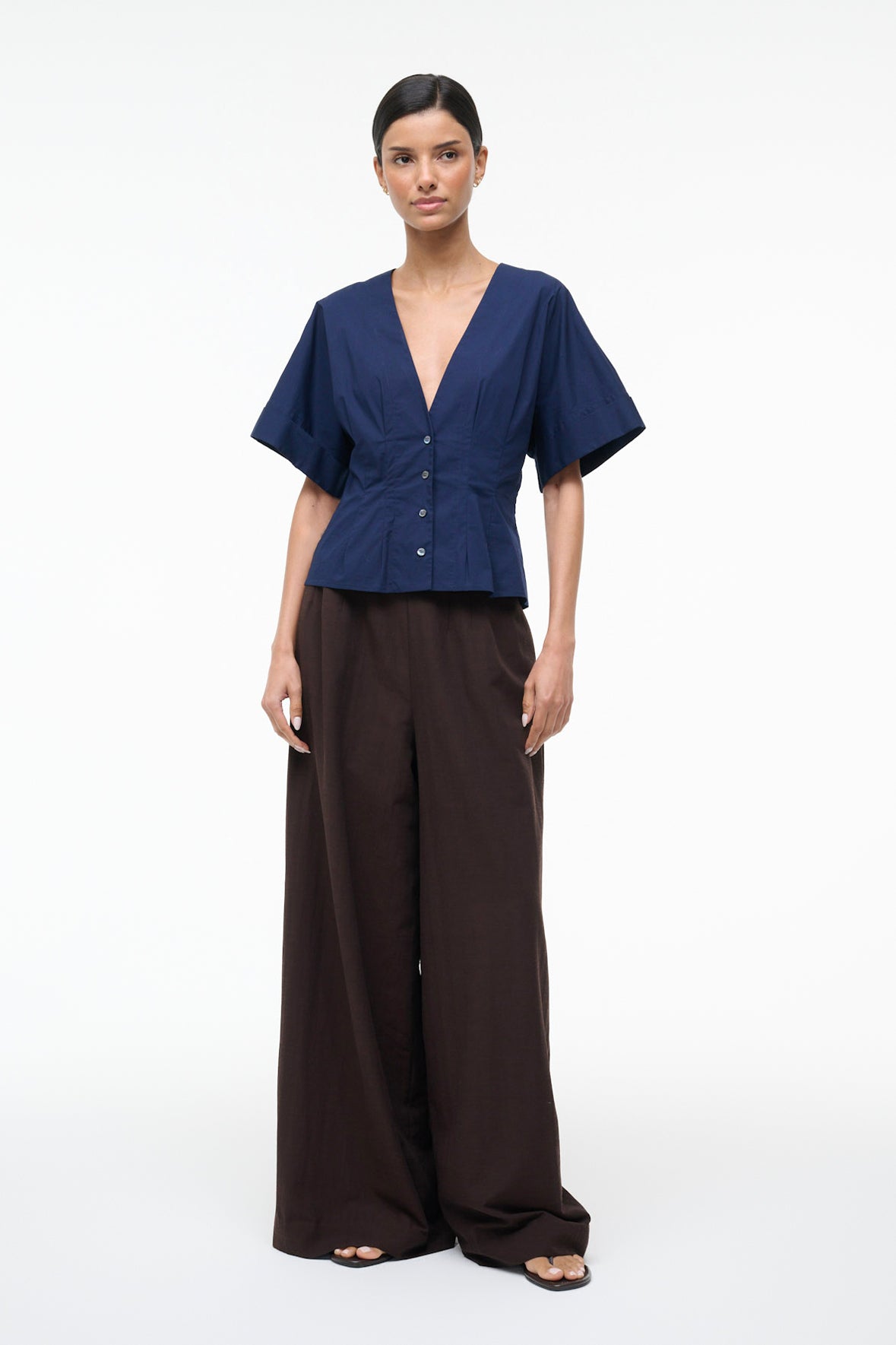 Woman wearing a navy top and brown pants on a white background
