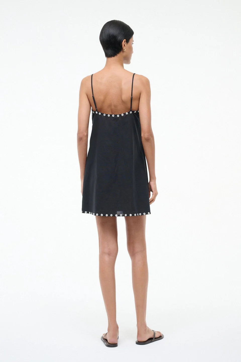 Woman wearing a black slip dress with pearl embellishments on a white background