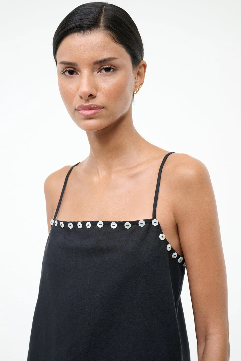Woman wearing a black dress with button embellishments on a white background
