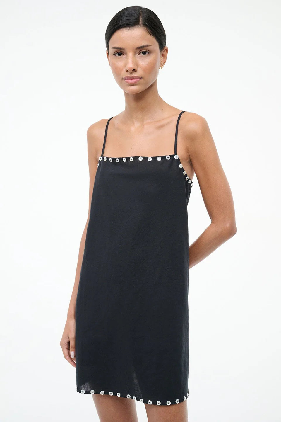 Woman wearing a black slip dress with white trim on a white background